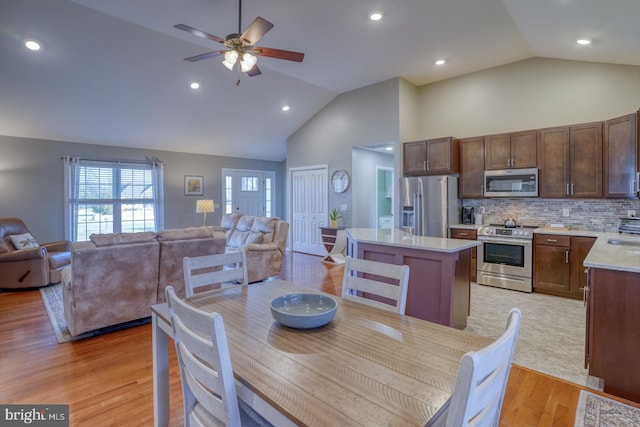 dining room featuring ceiling fan, sink, high vaulted ceiling, and light wood-type flooring