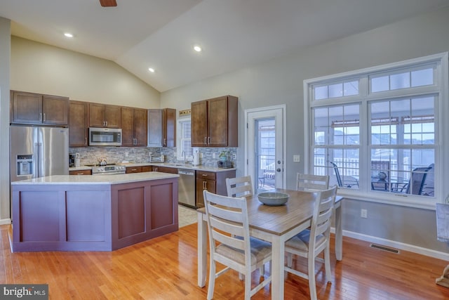 kitchen with stainless steel appliances, a kitchen island, decorative backsplash, vaulted ceiling, and light wood-type flooring