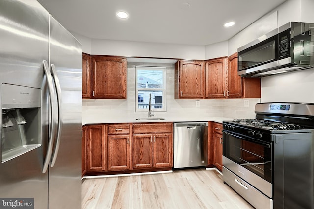 kitchen with stainless steel appliances, a sink, light wood-style flooring, and brown cabinets