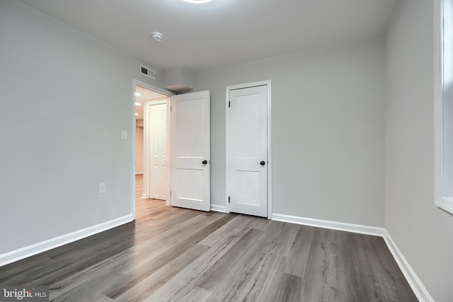 unfurnished bedroom featuring visible vents, a closet, baseboards, and wood finished floors