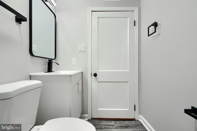 bathroom featuring toilet, baseboards, wood finished floors, and vanity