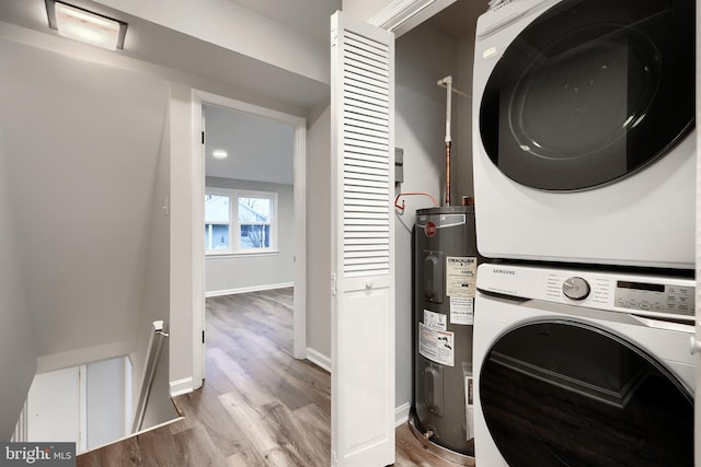 laundry area featuring stacked washer and clothes dryer, water heater, wood finished floors, laundry area, and baseboards