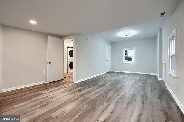 unfurnished living room with stacked washer and clothes dryer, visible vents, baseboards, and wood finished floors