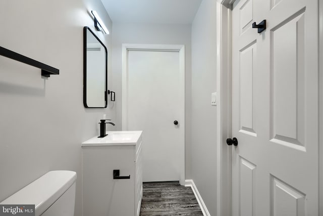 half bathroom with toilet, wood finished floors, vanity, and baseboards