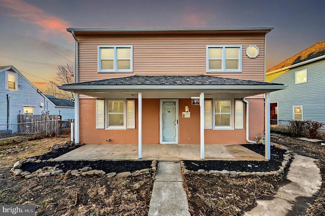 view of front of property with a shingled roof, covered porch, fence, and stucco siding