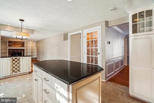 kitchen with white cabinetry, a kitchen island, built in shelves, a textured ceiling, and decorative light fixtures