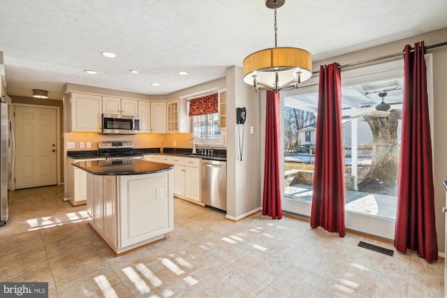 kitchen with appliances with stainless steel finishes, pendant lighting, sink, a center island, and a textured ceiling