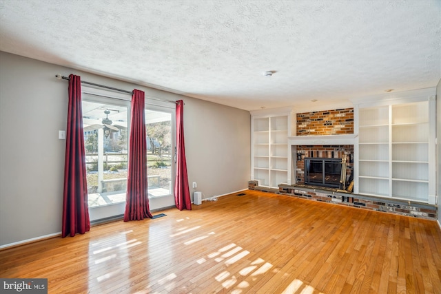 unfurnished living room with hardwood / wood-style flooring, built in shelves, a brick fireplace, and a textured ceiling