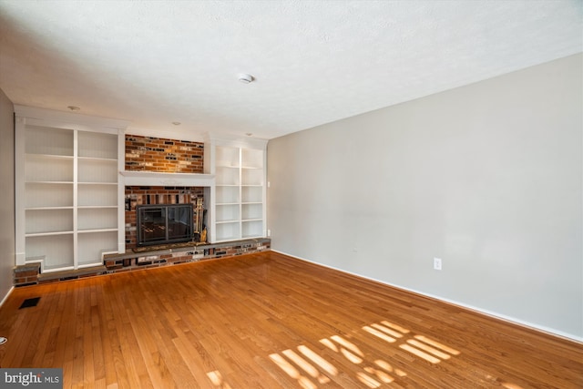 unfurnished living room featuring hardwood / wood-style flooring, a fireplace, built in features, and a textured ceiling