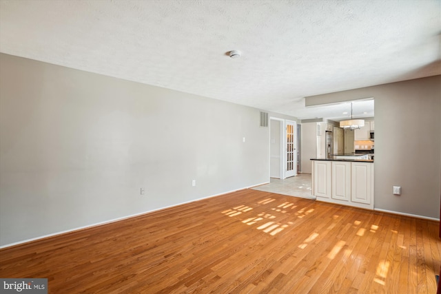 unfurnished living room with light hardwood / wood-style flooring and a textured ceiling