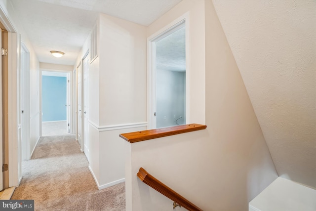 hall with light colored carpet and a textured ceiling