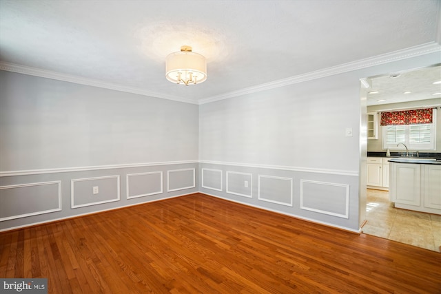 empty room with crown molding, sink, and light wood-type flooring