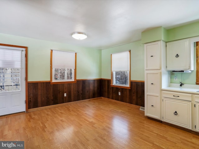 kitchen featuring wood walls, white cabinets, and light wood-type flooring