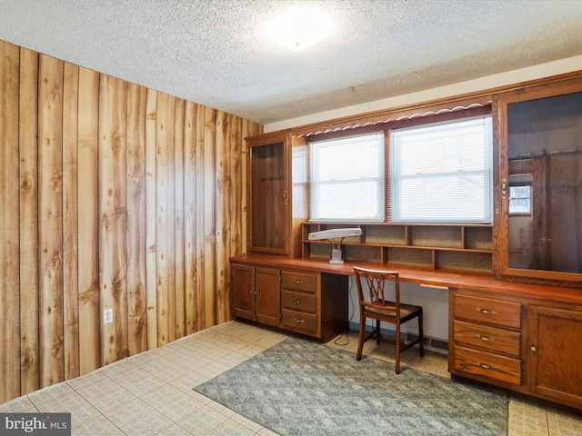 office area with built in desk, wooden walls, and a textured ceiling