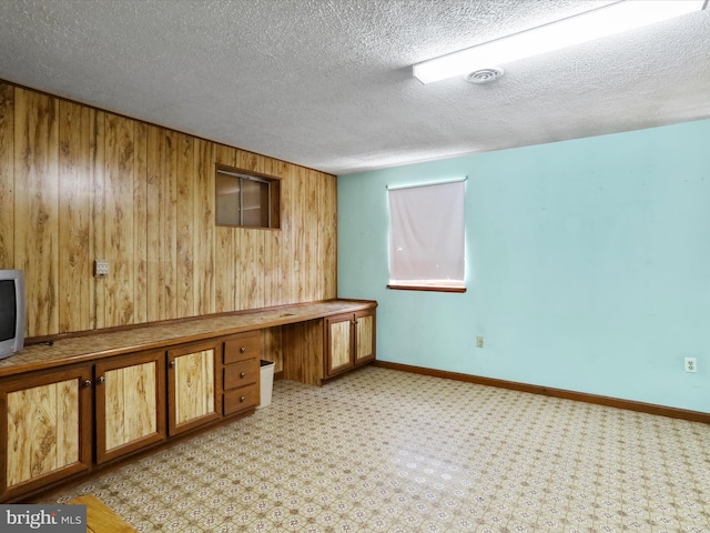 unfurnished office with built in desk, light colored carpet, a textured ceiling, and wood walls