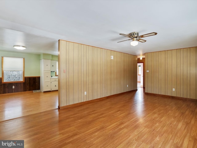 spare room featuring ceiling fan, light hardwood / wood-style floors, and wood walls