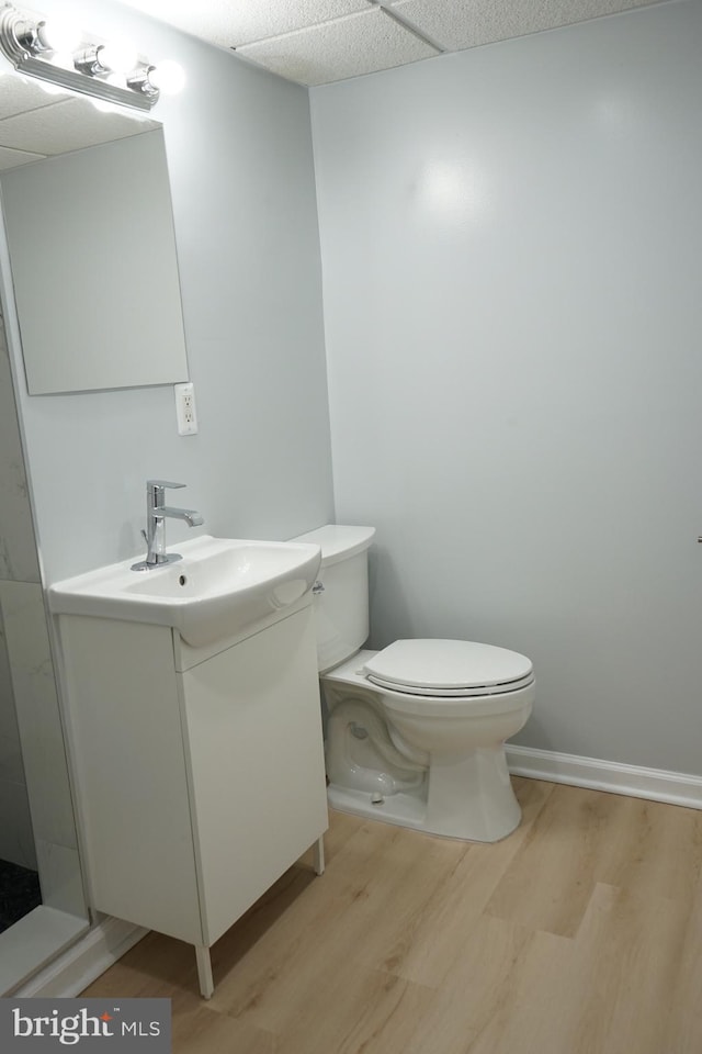 bathroom with toilet, vanity, wood finished floors, a drop ceiling, and baseboards