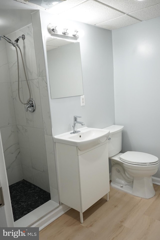 full bathroom with a tile shower, vanity, toilet, and wood finished floors