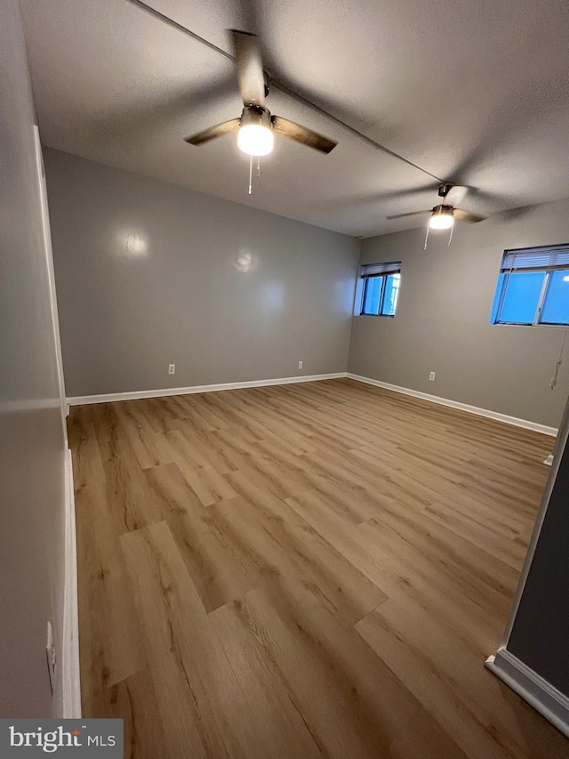 empty room with ceiling fan, a textured ceiling, wood finished floors, and baseboards