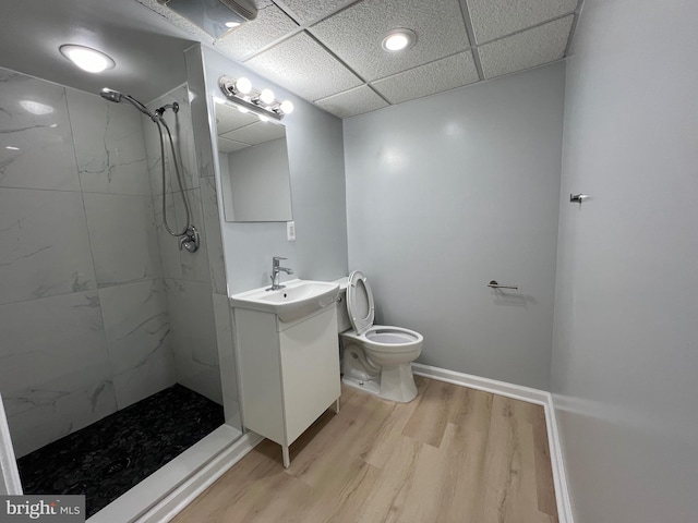 bathroom with toilet, wood finished floors, vanity, baseboards, and a tile shower