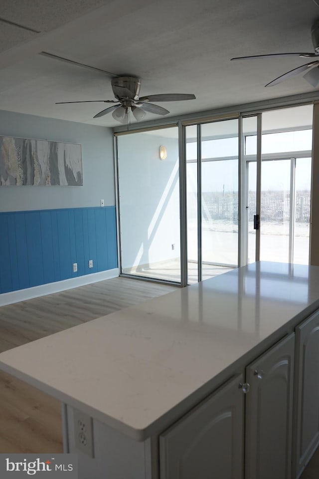 kitchen with a ceiling fan, light countertops, wood finished floors, and wainscoting