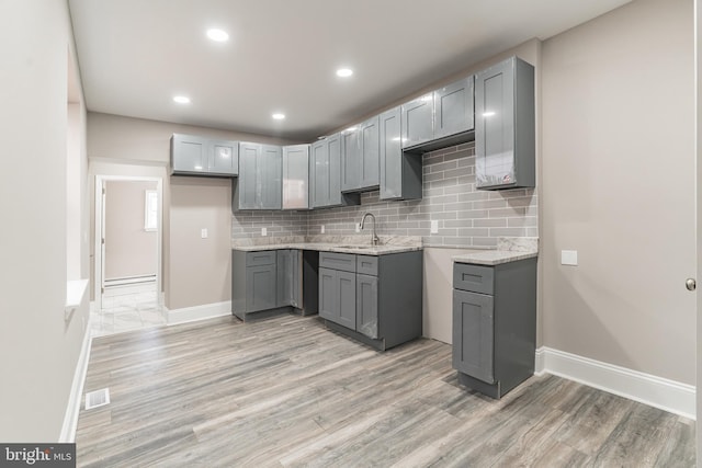 kitchen with light wood-type flooring, visible vents, gray cabinets, and a sink