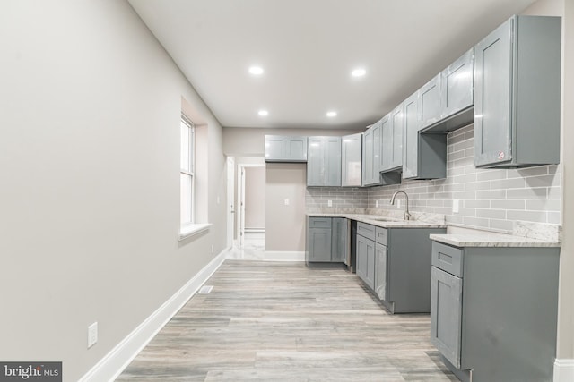 kitchen featuring tasteful backsplash, baseboards, light stone counters, gray cabinetry, and a sink