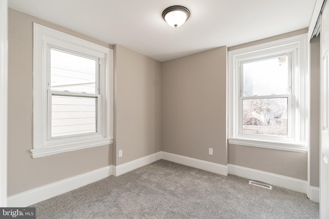 spare room with a healthy amount of sunlight, baseboards, and light colored carpet