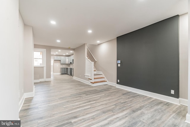 unfurnished living room featuring light wood-style flooring, stairs, baseboards, and recessed lighting