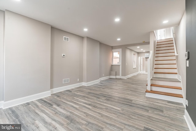 basement with light wood-type flooring, stairway, and visible vents