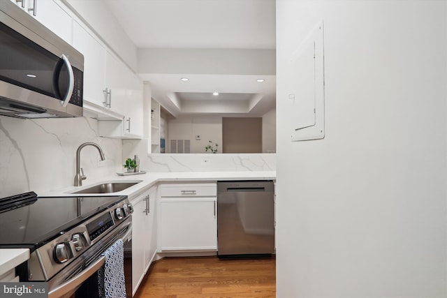 kitchen featuring sink, stainless steel appliances, light hardwood / wood-style floors, decorative backsplash, and white cabinets