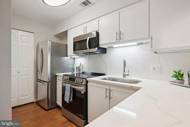 kitchen featuring sink, white cabinetry, appliances with stainless steel finishes, hardwood / wood-style floors, and decorative backsplash