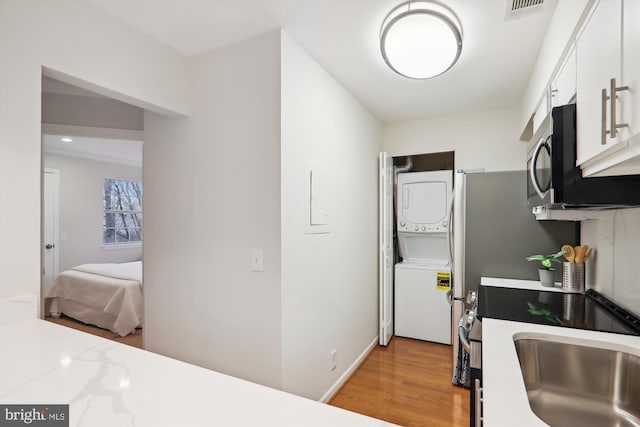 kitchen with stacked washing maching and dryer, sink, white cabinets, and light hardwood / wood-style floors