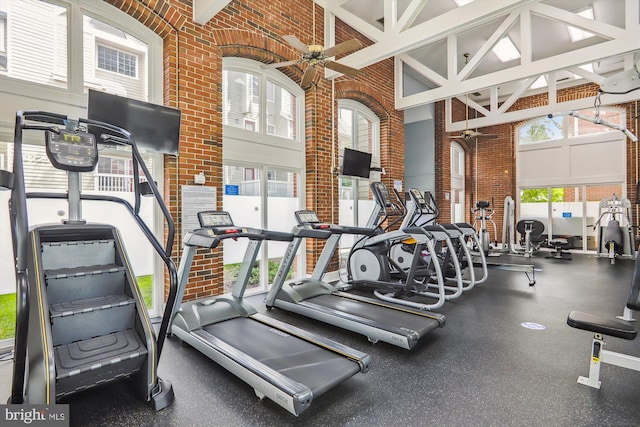 gym with a towering ceiling, ceiling fan, and brick wall