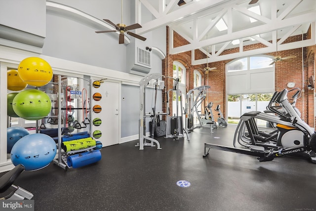 exercise room with ceiling fan, brick wall, and a high ceiling