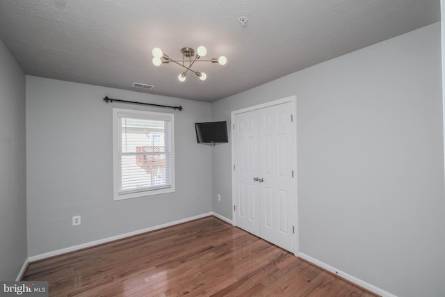 empty room featuring an inviting chandelier, wood-type flooring, and a textured ceiling