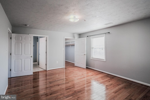 unfurnished bedroom with hardwood / wood-style flooring, a walk in closet, a closet, and a textured ceiling