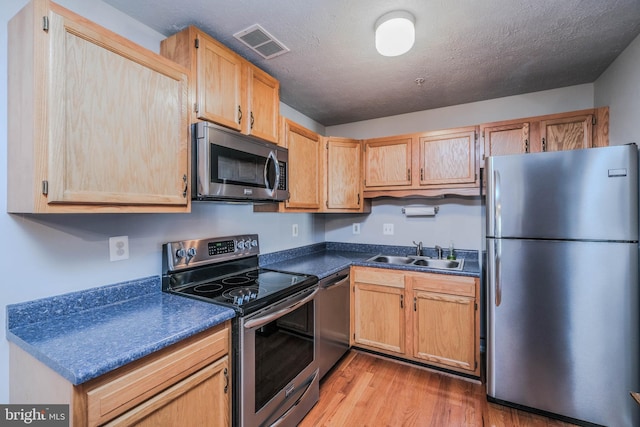 kitchen with light brown cabinetry, sink, light hardwood / wood-style floors, stainless steel appliances, and a textured ceiling