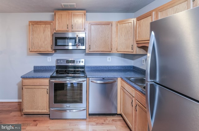 kitchen featuring stainless steel appliances, light brown cabinetry, light hardwood / wood-style floors, and a textured ceiling