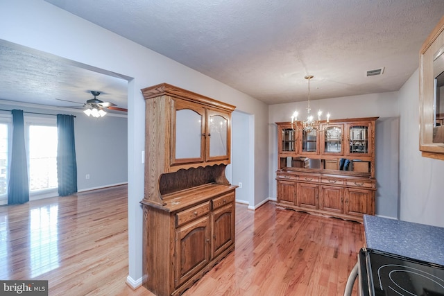 dining area with ceiling fan with notable chandelier, a textured ceiling, and light wood-type flooring