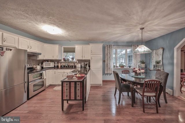 kitchen featuring wood-type flooring, appliances with stainless steel finishes, white cabinets, and decorative light fixtures