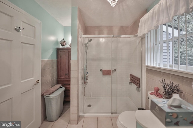 bathroom with tile walls, tile patterned flooring, walk in shower, toilet, and a textured ceiling