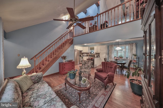 living room with ceiling fan, a towering ceiling, and light hardwood / wood-style floors