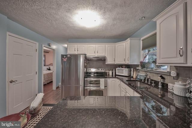 kitchen with sink, white cabinetry, dark stone countertops, stainless steel appliances, and tasteful backsplash