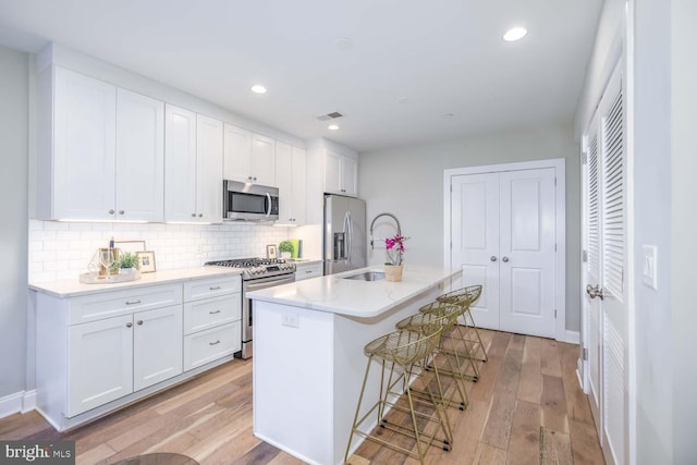 kitchen with stainless steel appliances, a breakfast bar, a center island with sink, and white cabinets