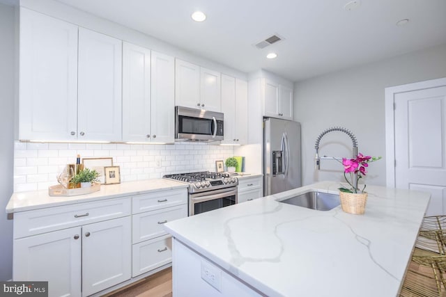 kitchen featuring an island with sink, sink, white cabinets, stainless steel appliances, and light stone countertops