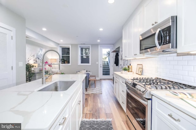 kitchen with sink, light stone counters, light wood-type flooring, stainless steel appliances, and white cabinets