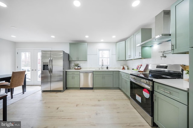 kitchen featuring green cabinets, stainless steel appliances, wall chimney range hood, and a sink