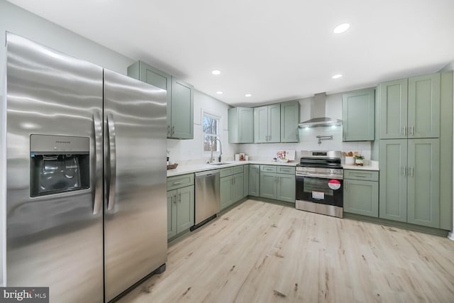 kitchen with green cabinetry, wall chimney exhaust hood, stainless steel appliances, light countertops, and a sink