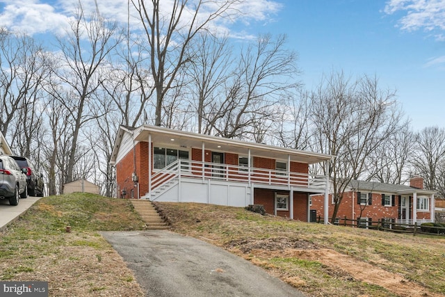 view of front facade featuring covered porch, driveway, brick siding, and stairway